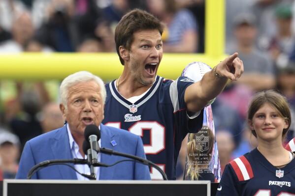 Former New England Patriots quarterback Tom Brady, second from left, points toward the audience as Patriots owner Robert Kraft, left, addresses the crowd as Brady's daughter Vivian, right, looks on during halftime ceremonies held to honor Brady at an NFL football game between the Philadelphia Eagles and the Patriots, Sunday, Sept. 10, 2023, in Foxborough, Mass. (AP Photo/Mark Stockwell)